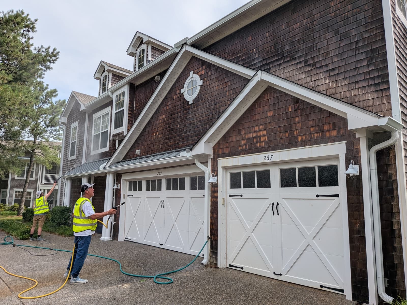Two Drone Precision Solutions crew members soft-washing the cedar-shake siding of a two-story home.