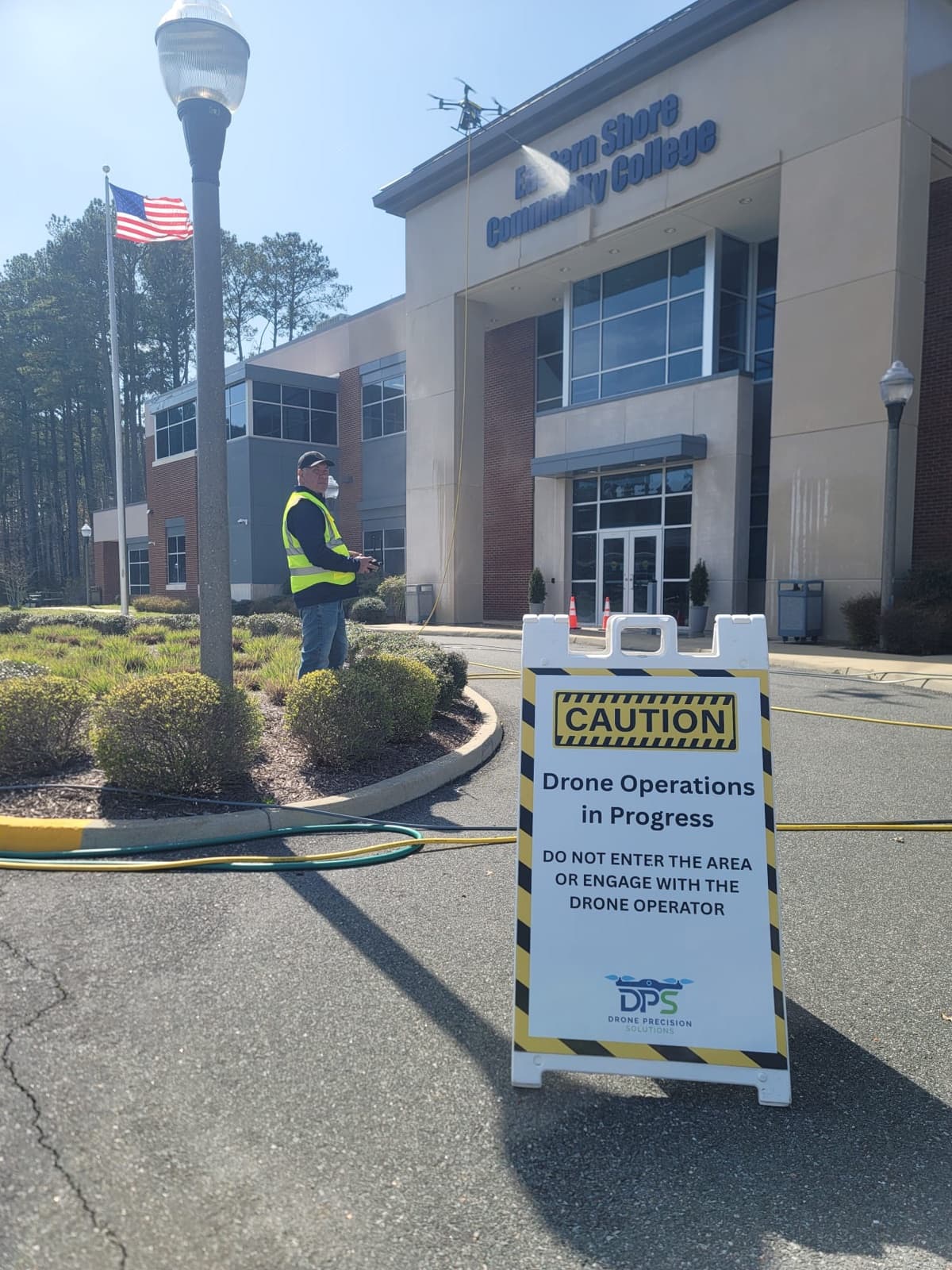 A cleaning drone soft-washing a building's upper facade from the air, the crew working safely from the ground