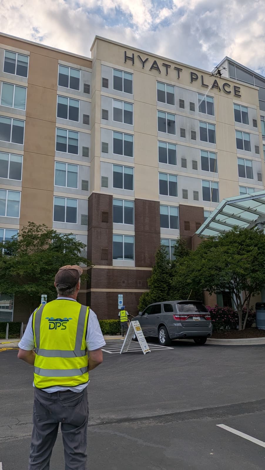 A Drone Precision Solutions pilot flying a cleaning drone up the facade of a multi-story Hyatt Place hotel